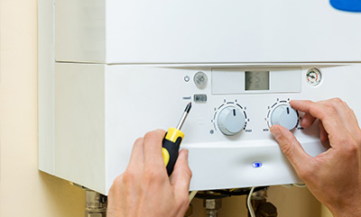 hands adjusting the settings on a white boiler unit with a screwdriver showing temperature control and digital display for efficient heating systems at home and plumbing tips for twenty degrees