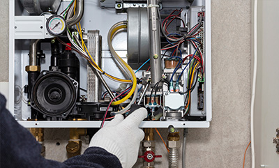 person wearing a glove inspecting wires and components inside a heating system with various connections and a pressure gauge focusing on gas and electricity system 19 components and maintenance
