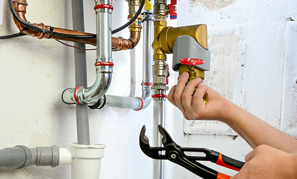 person using pliers to repair plumbing pipes and fixture in a home setting three maintenance tips
