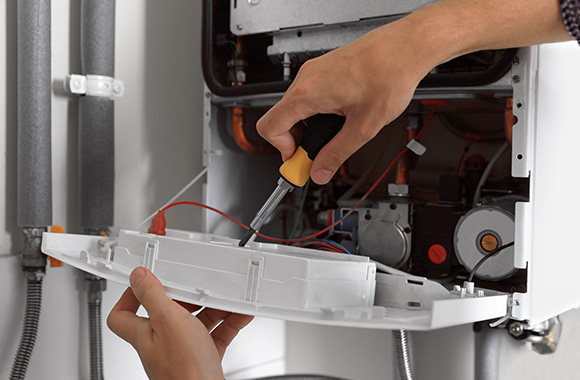 person repairing a gas boiler with a screwdriver in hand focused on maintenance steps for optimal function seven efficient repairs