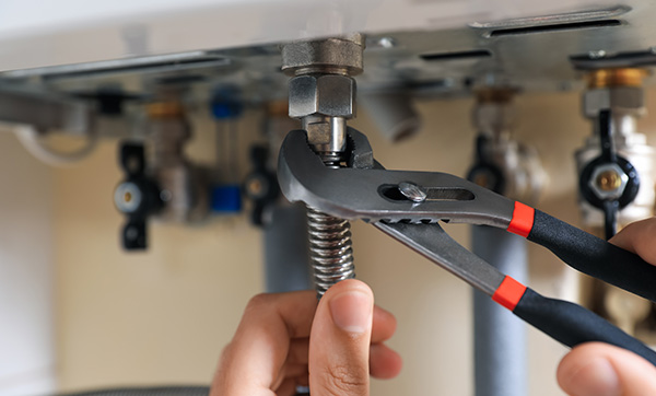 person using adjustable pliers to tighten a fitting under a sink with plumbing components visible including valves and pipes 14 plumbing tools and techniques