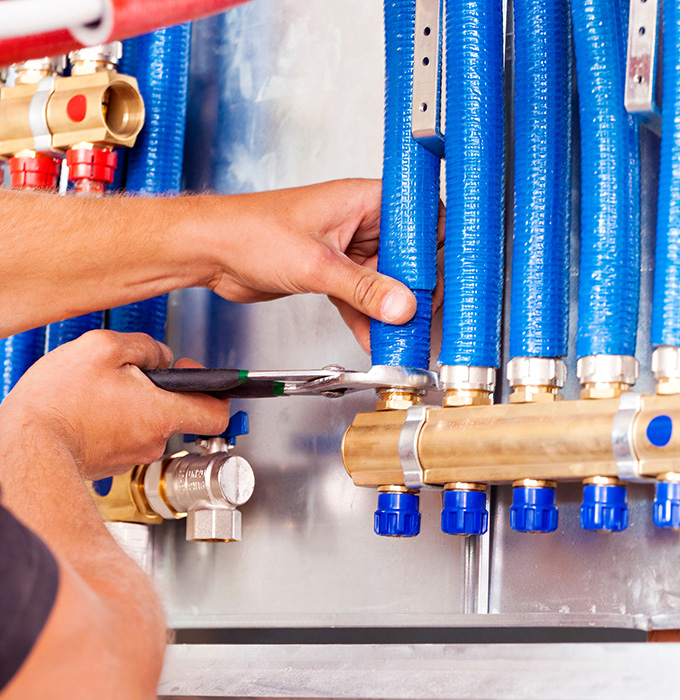 hand adjusting plumbing connections with blue hoses and brass fittings in a mechanical setup showcasing tools for six essential plumbing functions